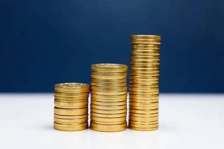Gráfico de barras ascendente com moedas de ouro empilhadas ao lado, representando crescimento financeiro.