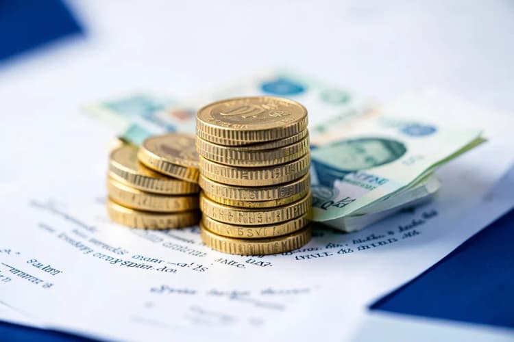 Uma pilha de moedas de ouro e notas de dinheiro em cima de um contrato.