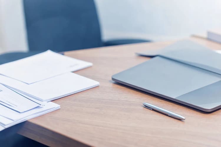 Mesa de escritório com documentos organizados, um laptop desligado e uma caneta, sugerindo planejamento e análise em M&A.