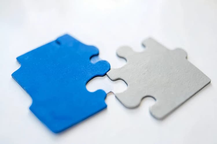 Duas peças de quebra-cabeça se encaixando perfeitamente, uma azul e outra cinza, representando a união de empresas.
